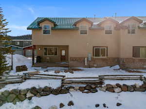 Back of property featuring a patio area, stone siding, stucco siding, and a standing seam roof