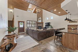 Living area featuring wood ceiling, stairway, a stone fireplace, a chandelier, and stone tile floors