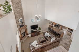 Carpeted living room with a stone fireplace, a towering ceiling, and a chandelier