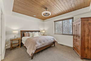 Bedroom featuring wood ceiling, light carpet, and a tray ceiling