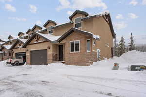 View of front of home featuring a garage, stucco siding, and stone siding