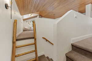 Stairway with wood ceiling, carpet floors, and vaulted ceiling