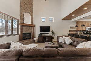 Carpeted living room featuring a stone fireplace and a high ceiling