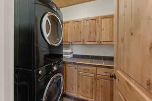Laundry room featuring stacked washer / dryer, cabinet space, and dark tile patterned flooring