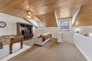 Rec room featuring wood ceiling, healthy amount of natural light, a ceiling fan, light carpet, and vaulted ceiling