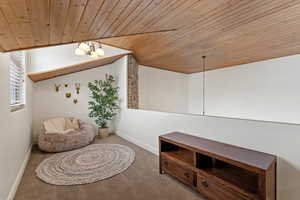 Living area featuring a chandelier, carpet flooring, wooden ceiling, and lofted ceiling