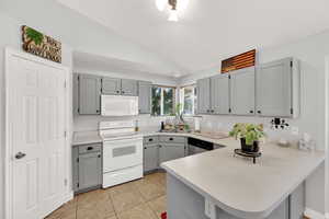 Kitchen with white appliances, gray cabinetry, light countertops, vaulted ceiling, and a peninsula