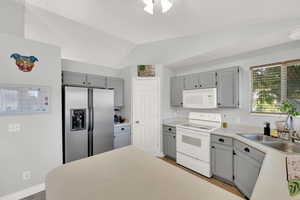 Kitchen featuring gray cabinets, white appliances, light countertops, and lofted ceiling