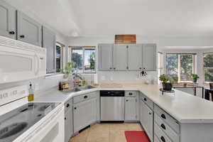 Kitchen with white appliances, a peninsula, light countertops, light tile patterned floors, and gray cabinetry