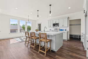 Kitchen with decorative backsplash, decorative light fixtures, a kitchen breakfast bar, white cabinetry, and a kitchen island with sink