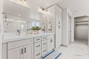 Full bath with light marble finish flooring, double vanity, a marble finish shower, a walk in closet, and recessed lighting