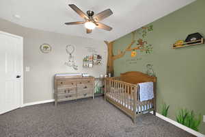 Bedroom featuring a nursery area, carpet floors, and a ceiling fan