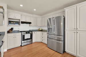 Kitchen with appliances with stainless steel finishes, light granite counters, backsplash, recessed lighting, and white cabinets