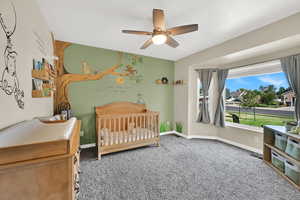Carpeted bedroom featuring a nursery area and a ceiling fan