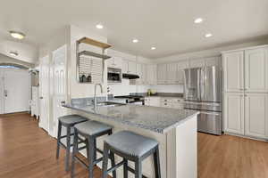 Kitchen featuring stainless steel & gas appliances, white cabinetry, a peninsula, light granite countertops, and light wood flooring