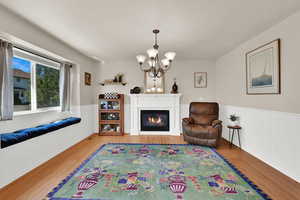 Formal dining or living room featuring wainscoting, a gas fireplace, a decorative wall, light wood flooring, and a chandelier