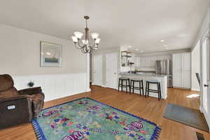 Formal dining or living area with light wood flooring, a chandelier, a wainscoted wall, recessed lighting, and a decorative wall