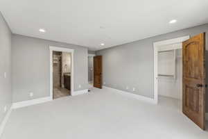 Unfurnished bedroom with recessed lighting, a spacious closet, light colored carpet, and ensuite bathroom