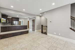 Kitchen with dark brown cabinets, recessed lighting, a peninsula, stainless steel fridge, and light stone counters