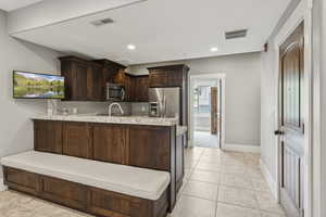 Kitchen with light countertops, a peninsula, dark brown cabinets, light tile patterned flooring, and appliances with stainless steel finishes