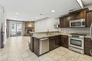 Kitchen featuring a peninsula, appliances with stainless steel finishes, dark brown cabinetry, open floor plan, and a fireplace