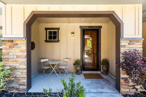Doorway to property featuring covered porch, board and batten siding, and stone siding