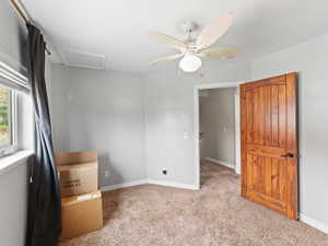 Unfurnished bedroom featuring carpet flooring, attic access, and a ceiling fan