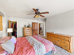 Carpeted bedroom with a spacious closet and a ceiling fan