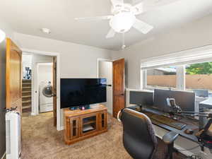 Home office with light colored carpet, washer / clothes dryer, and a ceiling fan