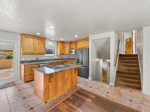 Kitchen with dark stone counters, appliances with stainless steel finishes, a center island, recessed lighting, and a textured ceiling