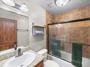 Full bathroom with vanity, shower / bath combination with glass door, and a textured ceiling