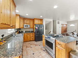 Kitchen with stainless steel range with gas cooktop, black refrigerator with ice dispenser, recessed lighting, white microwave, and open floor plan