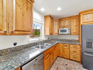 Kitchen with appliances with stainless steel finishes, dark stone countertops, recessed lighting, and brown cabinetry