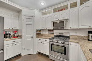 Kitchen featuring stainless steel appliances, white cabinets, light stone counters, and a textured ceiling