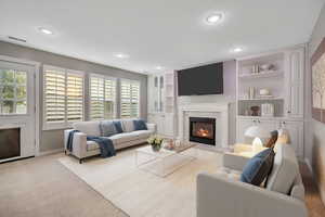Carpeted living room with a fireplace with flush hearth, built in shelves, recessed lighting. Virtually staged photo