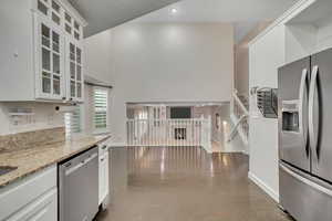 Kitchen with white cabinets, stainless steel appliances, a towering ceiling, concrete flooring, and light stone countertops