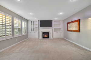 Unfurnished living room featuring light colored carpet, a fireplace with flush hearth, built in features, and recessed lighting