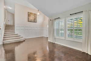 Spare room featuring a decorative wall, stairway, lofted ceiling, and wainscoting