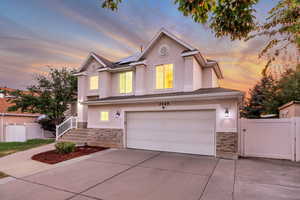 View of front of property featuring stone siding, an attached garage, roof mounted solar panels, and concrete driveway
