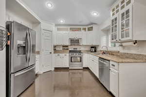 Kitchen with white cabinets, stainless steel appliances, finished concrete flooring, light stone countertops, and glass insert cabinets