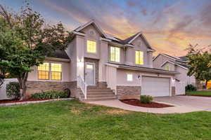 Traditional-style house featuring stone siding, concrete driveway, a front yard, stucco siding, and solar panels