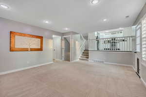 Unfurnished living room with light carpet, stairs, and recessed lighting