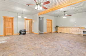 Unfurnished living room with a wood stove, a ceiling fan, and beam ceiling