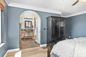Bedroom featuring a textured ceiling, light wood finished floors, ceiling fan, arched walkways, and ornamental molding