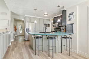 Kitchen featuring appliances with stainless steel finishes, light wood-style flooring, a textured ceiling, a kitchen breakfast bar, and pendant lighting
