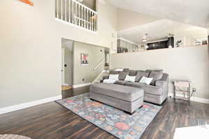 Living area with high vaulted ceiling, dark wood-style floors, and stairway