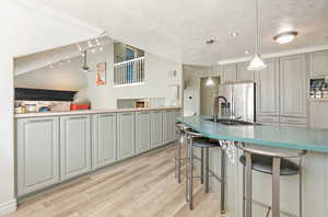 Kitchen with stainless steel fridge with ice dispenser, hanging light fixtures, light wood-type flooring, a textured ceiling, and a kitchen breakfast bar
