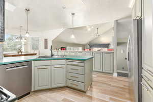 Kitchen with vaulted ceiling, appliances with stainless steel finishes, a textured ceiling, pendant lighting, and a peninsula
