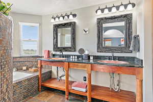 Bathroom with a bath, a textured ceiling, double vanity, and stone tile floors