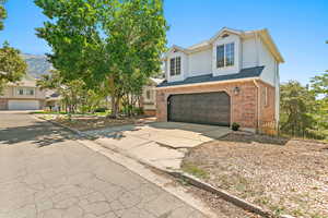 View of front facade featuring a garage, brick siding, concrete driveway, and a shingled roof